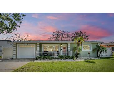 Charming single-story home featuring a white picket fence, attached garage, and freshly manicured lawn under a lovely pink sunset sky at 2025 Jefferson Ave, Dunedin, FL 34698