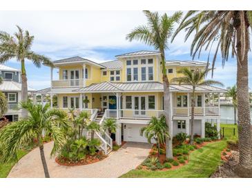 Stunning yellow waterfront home featuring multi-level balconies and lush tropical landscaping at 442 Midway Is, Clearwater Beach, FL 33767