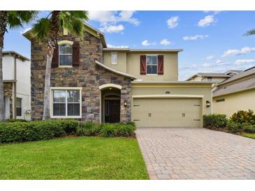 Charming home featuring a stone facade, well-manicured lawn, and a brick paved driveway leading to a two-car garage at 4544 Vermillion Sky Dr, Wesley Chapel, FL 33544