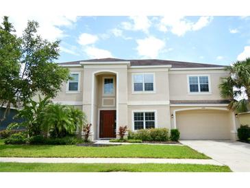 Beige two-story home with a well-manicured lawn, two-car garage, and mature landscaping at 11408 Scribner Station Ln, Lithia, FL 33547