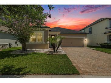 Charming single-Gathering home featuring a brick driveway, two-car garage, and mature landscaping under a dramatic sunset at 12322 Eagle Swoop Pl, Riverview, FL 33579