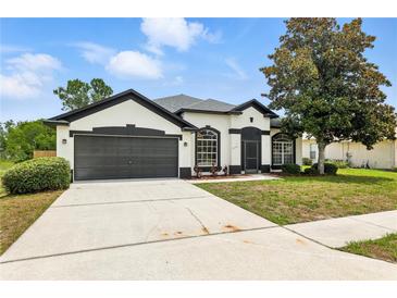 Charming one-story home boasts a well-manicured lawn, two-car garage, and classic stucco exterior with black trim at 5390 Greystone Dr, Spring Hill, FL 34609