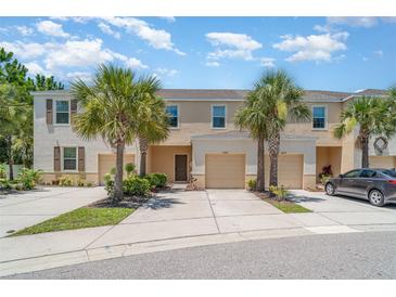 Townhouse exterior featuring a two-car garage, lush palm trees, and neatly landscaped front yard at 12841 Buffalo Run Dr, Gibsonton, FL 33534