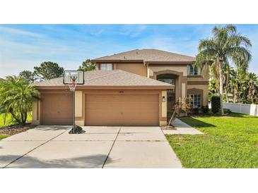 Two-story home featuring a three-car garage, basketball hoop, tropical trees, and a manicured lawn at 13003 Carlington Ln, Riverview, FL 33579