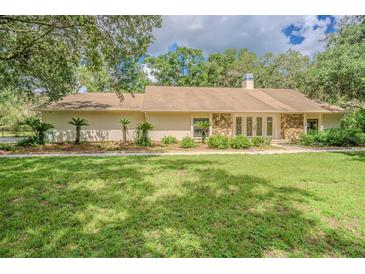 Inviting single-story home with a lush green lawn, mature trees, and decorative stone accents on the facade at 18110 30Th St, Lutz, FL 33559
