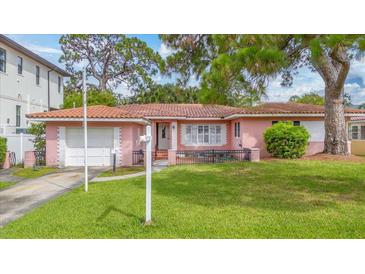 Charming pink home featuring a well-manicured front lawn, a mailbox, and a short driveway leading to an attached garage at 267 Snell Isle Ne Blvd, St Petersburg, FL 33704
