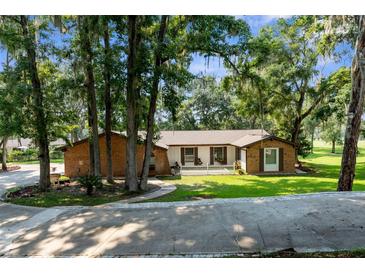 Charming single-story brick home with lush landscaping, mature trees, and a welcoming front porch at 23327 Christian Cir, Brooksville, FL 34601