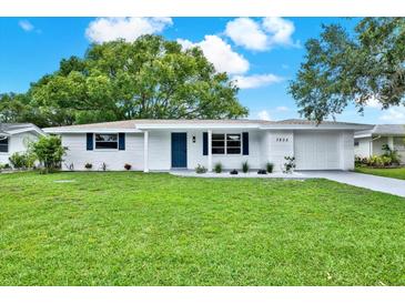Charming home featuring a manicured lawn, fresh paint, and stylish blue accents against a bright sunny sky at 7835 Wallaba Ln, New Port Richey, FL 34653