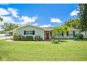 Charming home featuring a well-manicured lawn, a bright red front door, and lovely landscaping at 1857 N Belleair N Rd, Clearwater, FL 33764