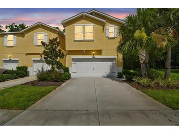 Charming yellow townhome with a two-car garage and well-maintained landscaping at 17880 Althea Blue Pl, Lutz, FL 33558