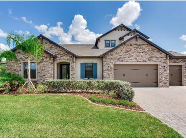 Beautiful stone home with a well-manicured lawn, palm tree and paved driveway on a sunny day at 6057 Marsh Trail Dr, Odessa, FL 33556