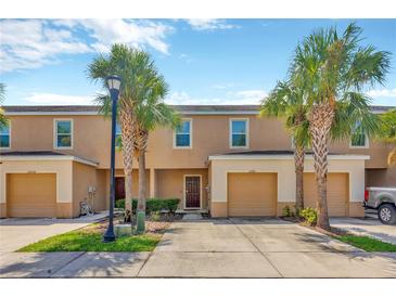 Inviting townhome featuring a two-car garage, lovely landscaping, and mature palm trees at 12710 Buffalo Run Drive, Gibsonton, FL 33534