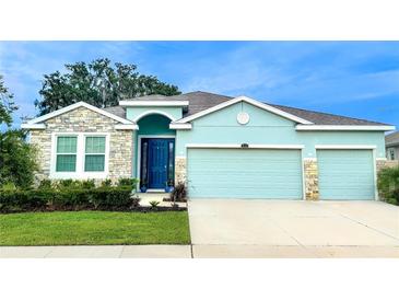 Charming single-Gathering home with a well-manicured lawn, stone accents, and a vibrant blue door at 10702 Laxer Cay Loop, San Antonio, FL 33576