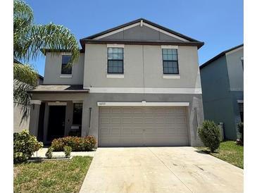 Two-story home featuring a gray exterior, a two-car garage, and a well-manicured lawn with mature landscaping at 10221 Carloway Hills Dr, Wimauma, FL 33598
