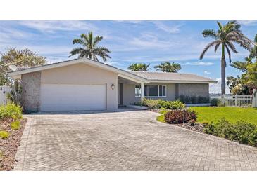 Charming single-story home with a brick driveway, lush landscaping, and a two-car garage at 11055 7Th E St, Treasure Island, FL 33706