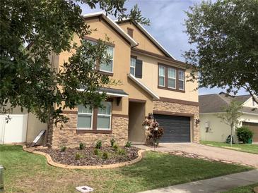 Tan two-story home featuring stacked stone accents, manicured landscaping, and a two-car garage at 2588 Bartolo Dr, Land O Lakes, FL 34639