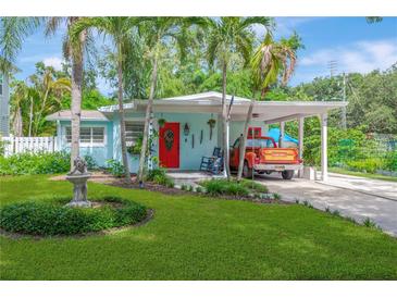 Charming home with a bright red door, lush green lawn, a covered carport, and tropical landscaping at 1042 S Sterling Ave, Tampa, FL 33629