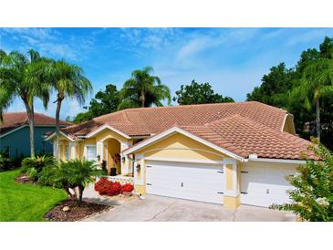 Charming yellow home featuring a tile roof, three-car garage, and lush tropical landscaping with mature palm trees at 1358 Forestedge Blvd, Oldsmar, FL 34677