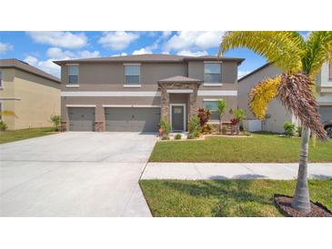 Two-story home featuring a three-car garage, stone accents, and beautifully landscaped front yard at 9456 Channing Hill Dr, Sun City Center, FL 33573