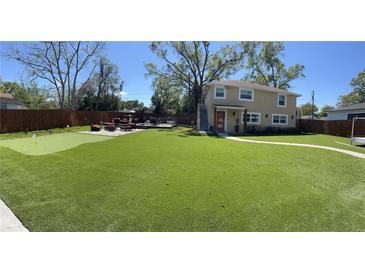 A sprawling green backyard featuring a putting green, deck with outdoor furniture, and a two-story home in the background at 4438 58Th N Ave, St Petersburg, FL 33714