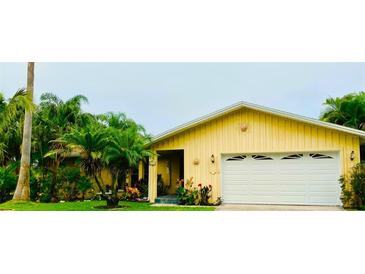 Charming yellow home featuring a two-car garage, lush landscaping, and great curb appeal at 1964 Arvis E Cir, Clearwater, FL 33764