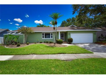 Charming home featuring a manicured lawn, palm trees, and a two-car garage at 10799 Harborside Dr, Largo, FL 33773