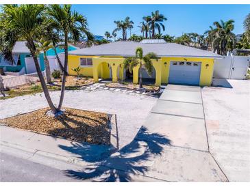Charming yellow home features a one car garage, an arched entryway, and lush tropical landscaping at 855 Boca Ciega Isle Dr, St Pete Beach, FL 33706