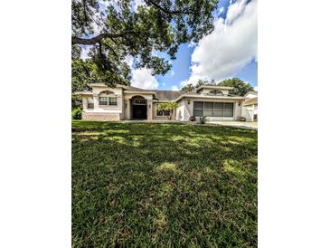 Charming single-story home featuring a lush lawn, attached garage, and elegant stucco exterior with a well-manicured landscape at 8088 Spanish Oak Dr, Spring Hill, FL 34606