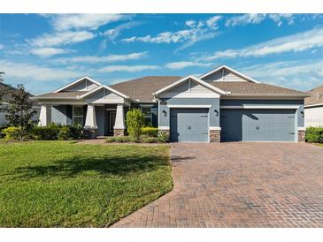 Two-story home with gray exterior, three car garage, and a brick driveway at 19907 Tattnall Way, Brooksville, FL 34601