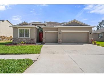 Charming single-story home featuring a red front door, neutral paint, stone accents, and an attached two-car garage at 13822 Bee Tree Ct, Hudson, FL 34669