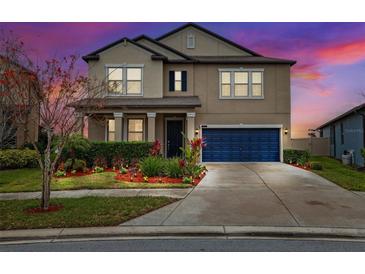 Charming two-story home featuring a well-manicured lawn, vibrant flower beds, and a stylish blue garage door at 9173 Shadyside Ln, Land O Lakes, FL 34637