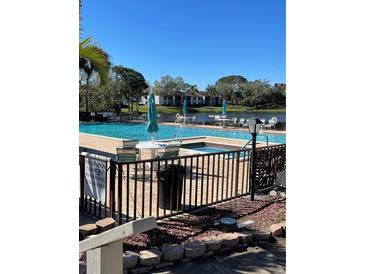 Large community pool with brick surround, lounge chairs and umbrellas on a sunny day at 2642 Pine Ridge S Way # B2, Palm Harbor, FL 34684