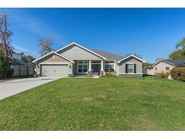 Charming home features a lush green lawn, two-car garage, and covered porch with stone accents at 5139 Jenson Ave, Spring Hill, FL 34608