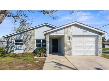 Charming home featuring a stone facade, an attached garage, and freshly manicured lawn at 13726 Michelle Ave, Hudson, FL 34667