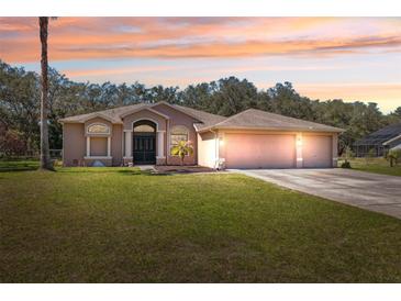Charming single-story home with a three-car garage and a well-manicured lawn under a beautiful sunset sky at 18251 East Rd, Hudson, FL 34667