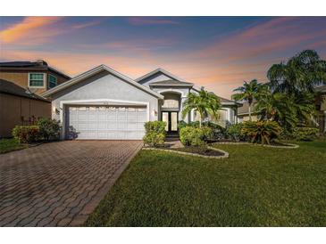 Beautiful single-Gathering home with lush landscaping, brick driveway, and two-car garage at sunset at 215 Arbor Woods Cir, Oldsmar, FL 34677