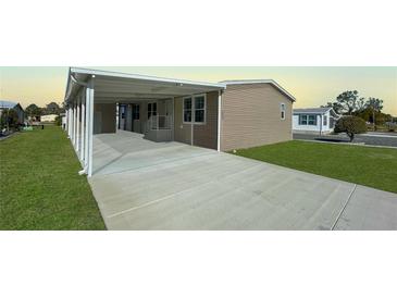 Tan home exterior with a covered carport, grassy lawn, and a concrete driveway at 9896 Scepter Ave, Brooksville, FL 34613