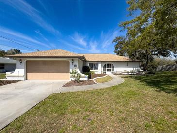 Well maintained one-story home with a tan two-car garage door, mature landscaping, and curved walkway at 8367 Apple Orchard Rd, Spring Hill, FL 34608