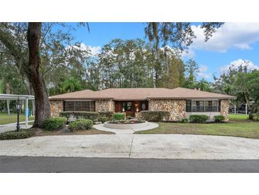 Charming stone home with a circular driveway, mature trees, and manicured landscaping offers great curb appeal at 19019 3Rd Ne St, Lutz, FL 33549