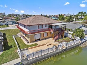 Two-story waterfront home featuring a backyard patio, fenced yard and expansive balconies on the upper level at 13820 Plumosa Ave, Hudson, FL 34667