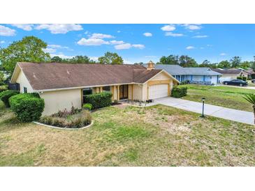 Single-story home features a well-manicured lawn and attached two car garage on a sunny day at 11256 Holbrook St, Spring Hill, FL 34609