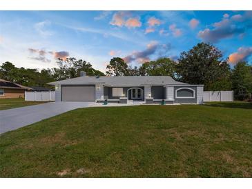 Charming single-story home with a well-manicured lawn, gray exterior, and an attached two-car garage at dusk at 1156 Battersea Ave, Spring Hill, FL 34609
