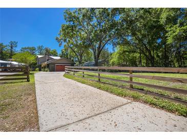 Long concrete driveway leading up to a two story home with a red garage door and mature trees at 28330 Peterson Camp Rd, Brooksville, FL 34601