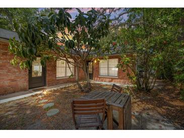 Secluded brick patio with wooden table and chairs, surrounded by lush greenery and a charming brick exterior at 5417 Carlton Rd, New Port Richey, FL 34652
