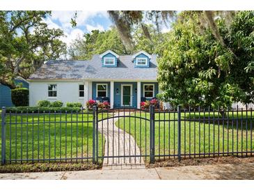 Charming cottage-style home with a well-manicured lawn, dark metal fence, and lush landscaping at 417 Inness Dr, Tarpon Springs, FL 34689