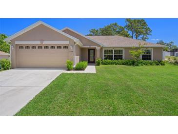 Well-maintained single-story home featuring a manicured lawn, attached two-car garage, and meticulously designed landscaping at 11310 Limpkin Rd, Weeki Wachee, FL 34614