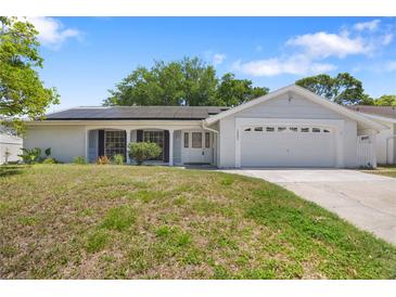 Charming single-story home with a two-car garage, well-maintained lawn, and solar panels on the roof at 12204 Pepper Mill Dr, Hudson, FL 34667