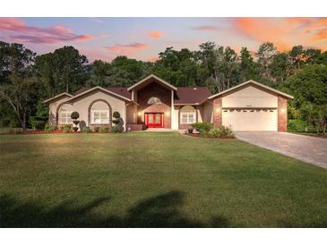 Charming single-story home showcasing a well-manicured lawn and inviting red double-door entry at 4469 Lake In The Woods Dr, Spring Hill, FL 34607