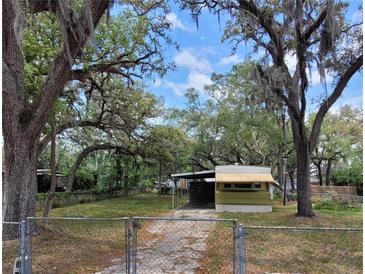 Exterior view of a one-story home with beautiful mature trees, a carport, and a chain link fence at 9441 Teak St, New Port Richey, FL 34654