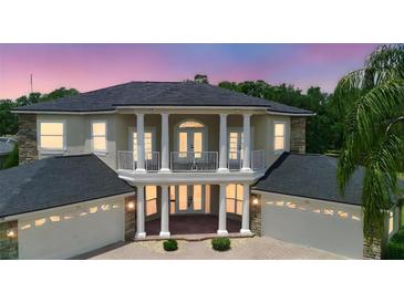 Elegant two-story home featuring white columns, a balcony, a dark roof, and a three-car garage at 15906 Prince William Pl, Odessa, FL 33556